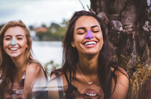 Two friends smiling wearing Nöz’s colorful eco friendly sunscreen in shades blue and purple.